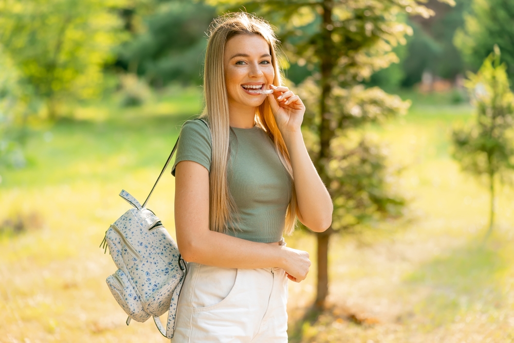 Young woman placing a clear dental retainer in her mouth outdoors after full-mouth reconstruction in Virginia Beach 