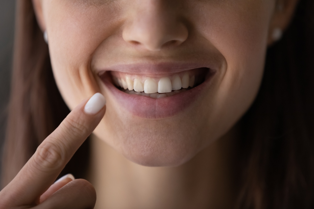 Happy girl showing toothy smile, pointing finger at healthy white teeth. Clinic patient satisfied with dentist service, enamel cleaning, whitening, dental care, correction. Cropped shot, close up