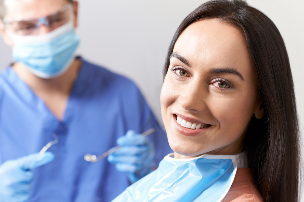 Female patient smiling confidently in dental chair with dentist preparing for Virginia Beach sedation dentistry procedure at The Foleck Center