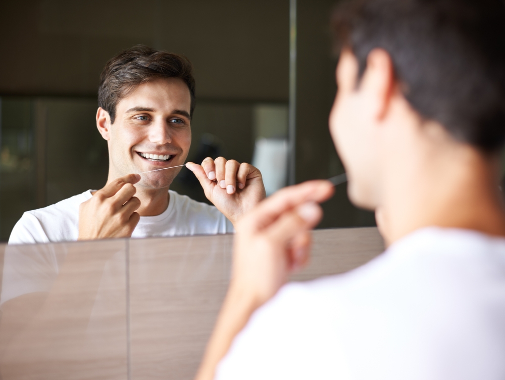 At-Home Flossing Routine: Hampton Kecoughtan Patient Man flossing his teeth in the bathroom mirror as part of his at-home dental care routine, a Hampton Kecoughtan patient
