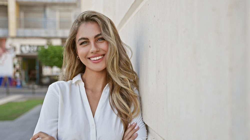 Confident smile, cosmetic dentistry in the Williamsburg community Woman with long wavy hair smiling confidently outdoors, cosmetic dentistry results in the Williamsburg community