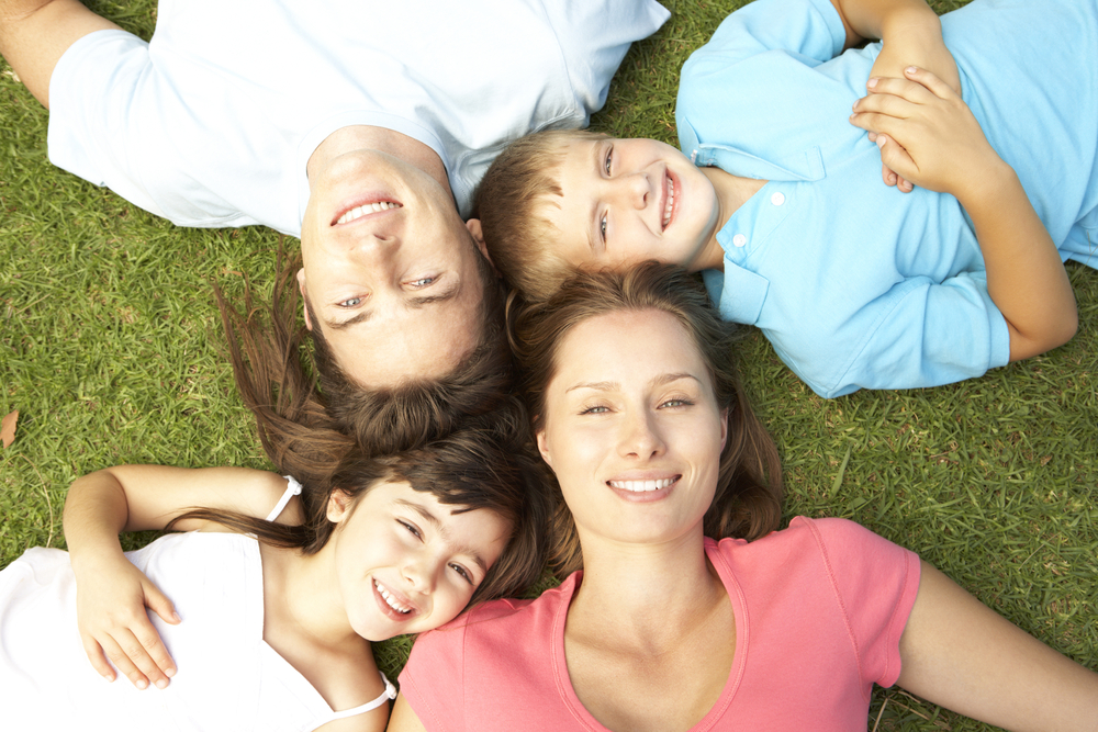 Family of four smiling together on the grass after gum disease care in the Norfolk community 