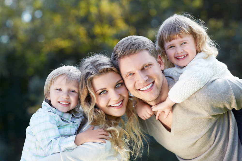 Healthy family smiles: dental care in the Norfolk community Family piggybacking together outdoors, reflecting the healthy smiles families enjoy in the Norfolk community