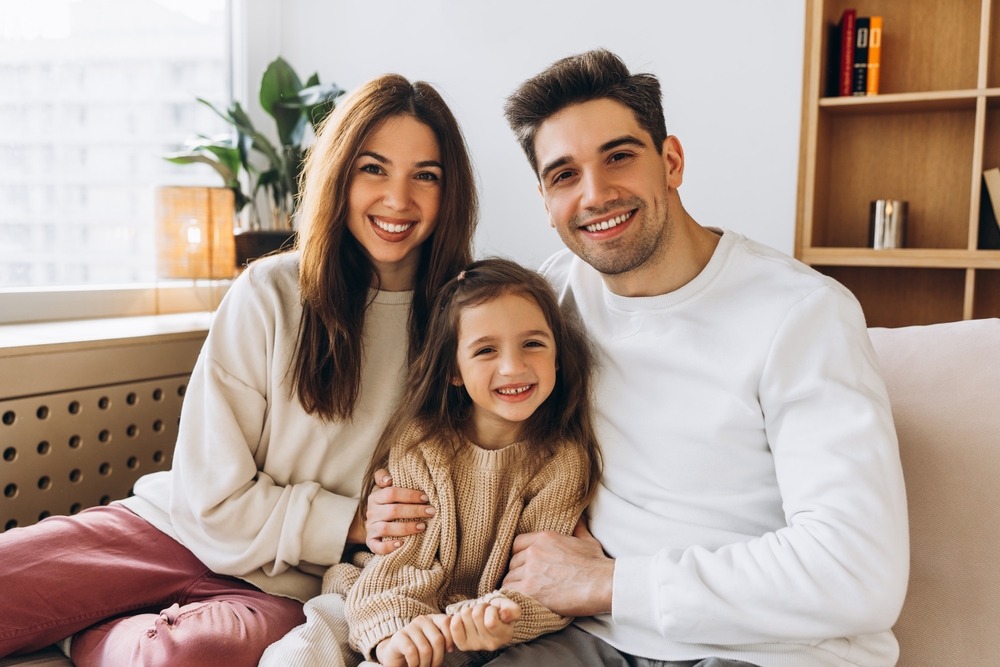Comprehensive care for the whole family in Hampton Roads Smiling mother, father, and daughter sitting together on a couch at home