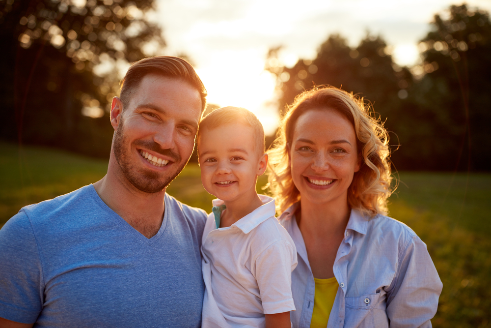 Young Family's Healthy Smiles: Norfolk Dental Fillings Patients Smiling young family outdoors together after a dental filling visit at The Foleck Center in Norfolk