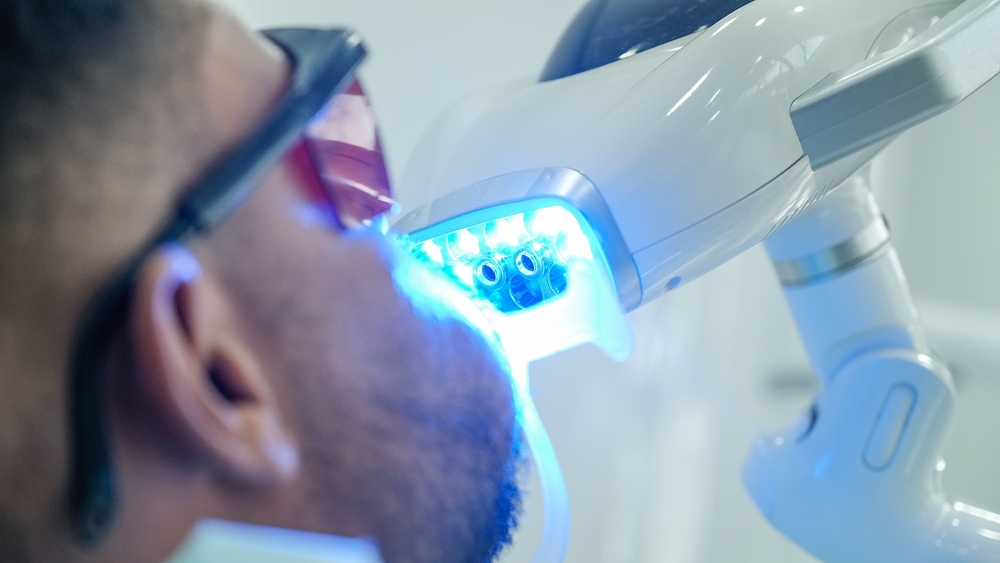 The teeth whitening machine with a blue light is being used on the male patient in the dental clinic.