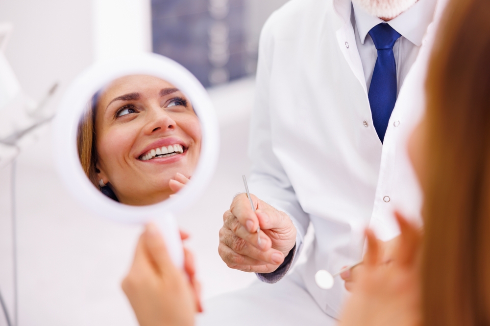 Patient reviewing smile transformation after cosmetic dentistry at The Foleck Center, Virginia Beach Female patient admiring her smile results in a hand mirror after cosmetic dentistry treatment at The Foleck Center in Virginia Beach