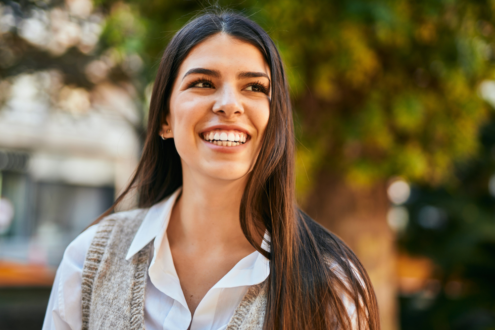 Young woman smiling outdoors with straight teeth after Invisalign treatment in the Kempsville community 