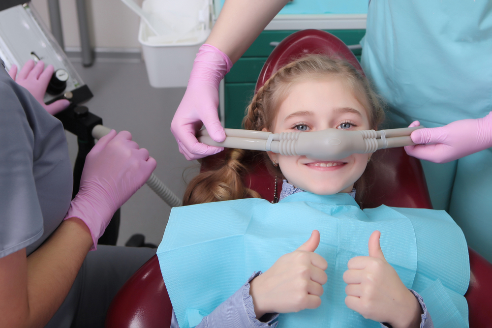 Young girl giving a thumbs-up while comfortable under sedation during a dental visit in Norfolk 