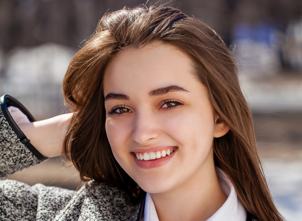 Confident smile, full mouth reconstruction in Hampton Roads Young woman with brown hair smiling outdoors in a winter setting