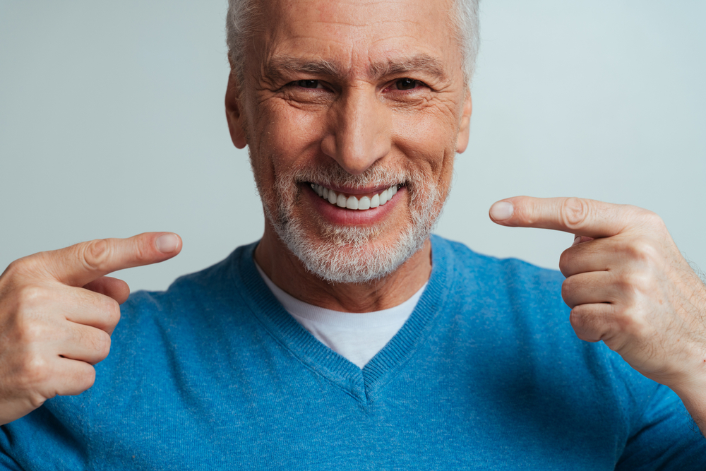 Smiling senior man pointing to his straight, white teeth after orthodontic treatment in Virginia Beach 