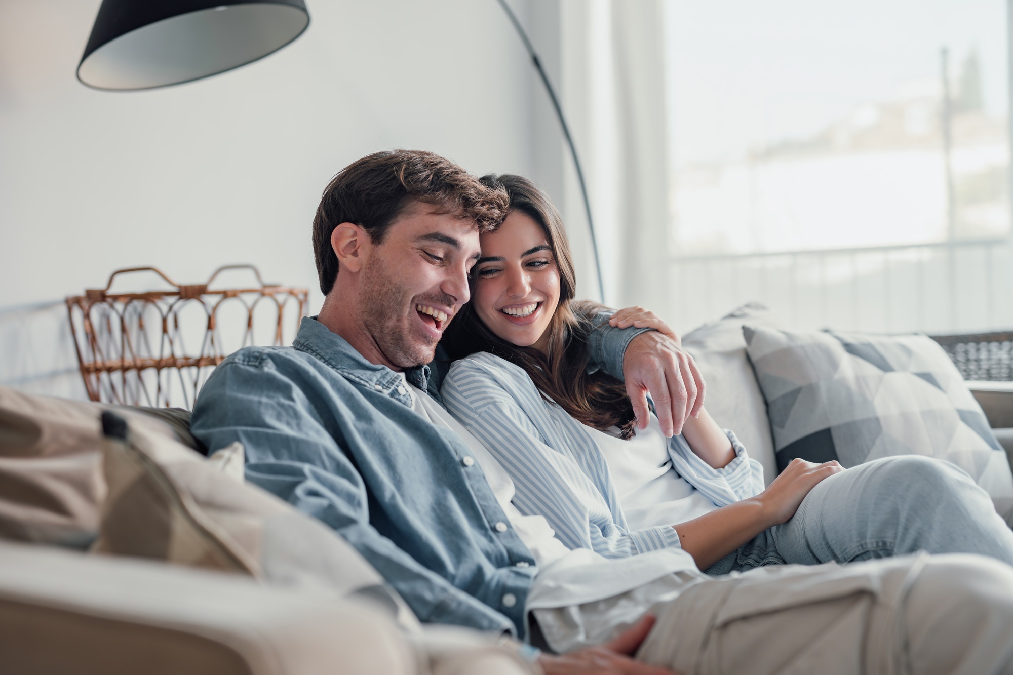 Comfortable, confident smiles: full mouth reconstruction in Hampton Roads Man and woman laughing together while sitting on a couch at home