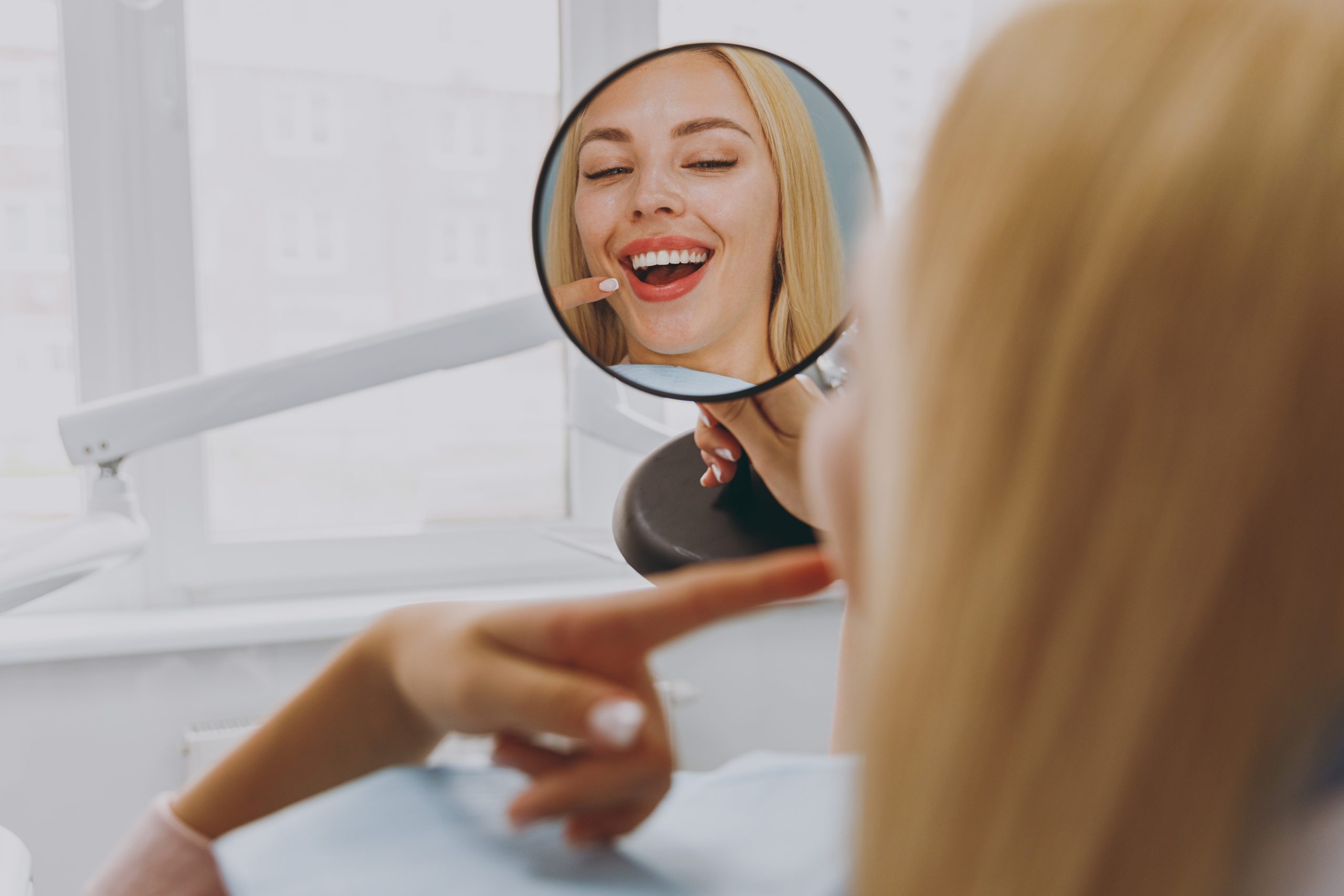 Woman admiring her smile in a hand mirror after dental bonding at The Foleck Center, Norfolk, VA 