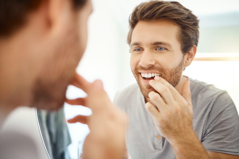 Man checking his smile in the mirror after dental implant treatment in Virginia Beach 