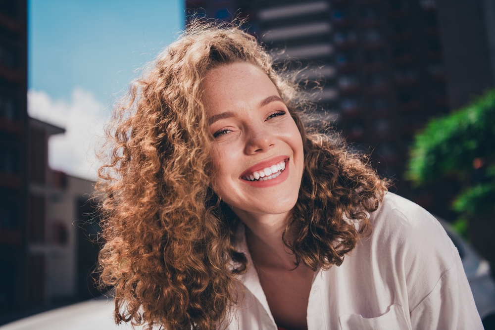 Confident smile following gum disease treatment at The Foleck Center in Virginia Beach, Norfolk, and Hampton Young woman smiling confidently outdoors after periodontal treatment at The Foleck Center in Hampton Roads