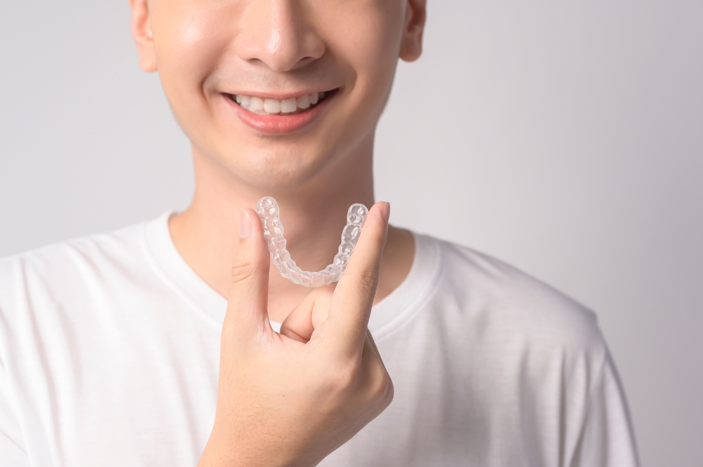 Invisalign clear aligner tray, The Foleck Center, Norfolk, VA Young man holding a clear Invisalign aligner tray near his smile at The Foleck Center, Norfolk, VA