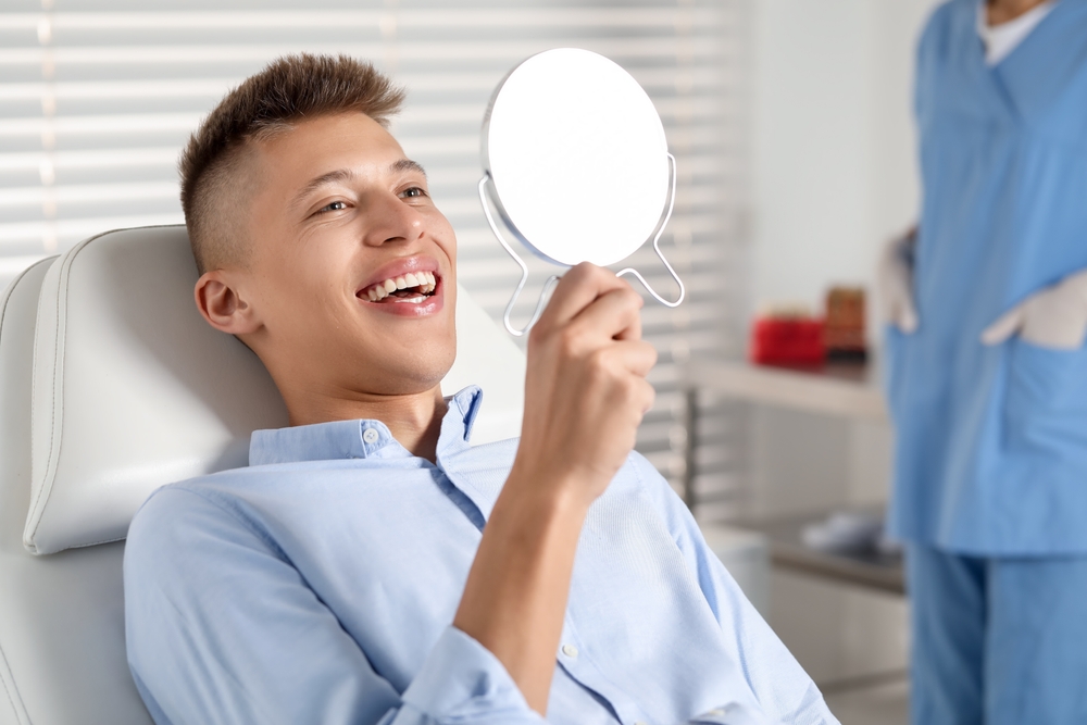 Young man smiling while reviewing his dental bonding results in a mirror at The Foleck Center, Norfolk, VA 